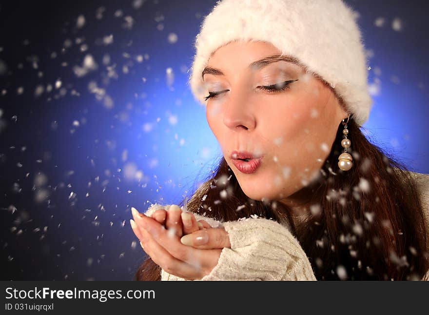 Cute young woman blows snowflakes