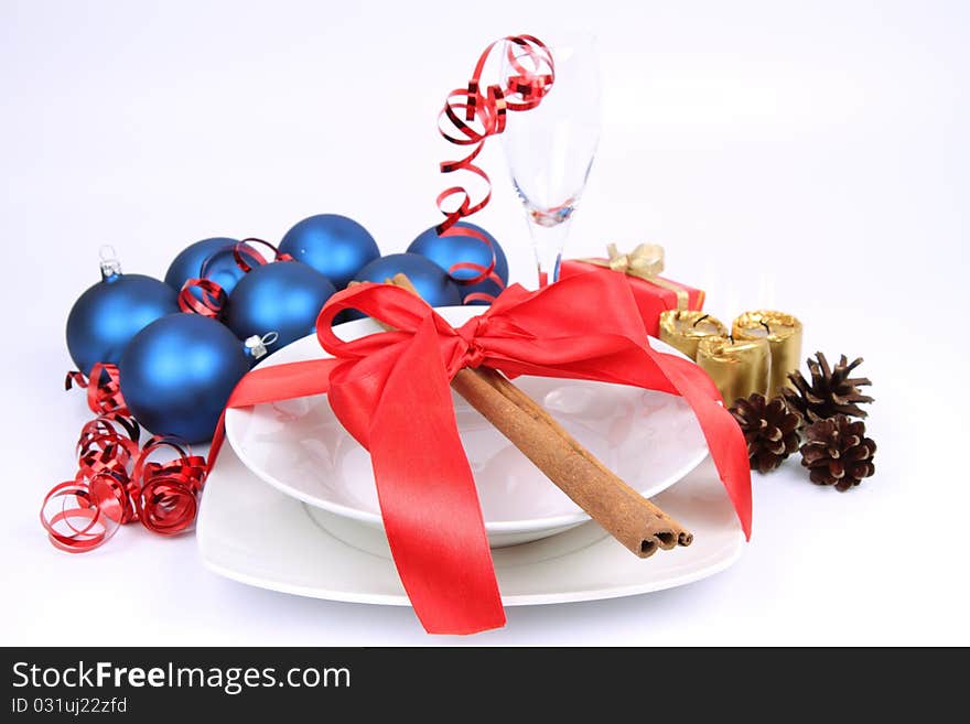 Christmas or New Year's setting - a plate decorated with cinnamon sticks and ribbon, a champagne glass, christmas balls, candles, gift and cones