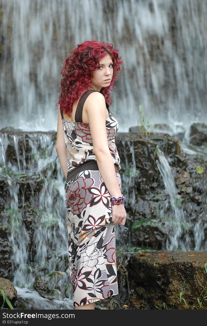 An attractive teenage woman walking near a fast flowing waterfall. An attractive teenage woman walking near a fast flowing waterfall.