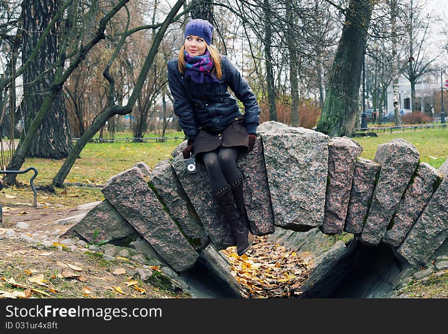 A girl in an autumn city park sits on stone rails. A girl in an autumn city park sits on stone rails