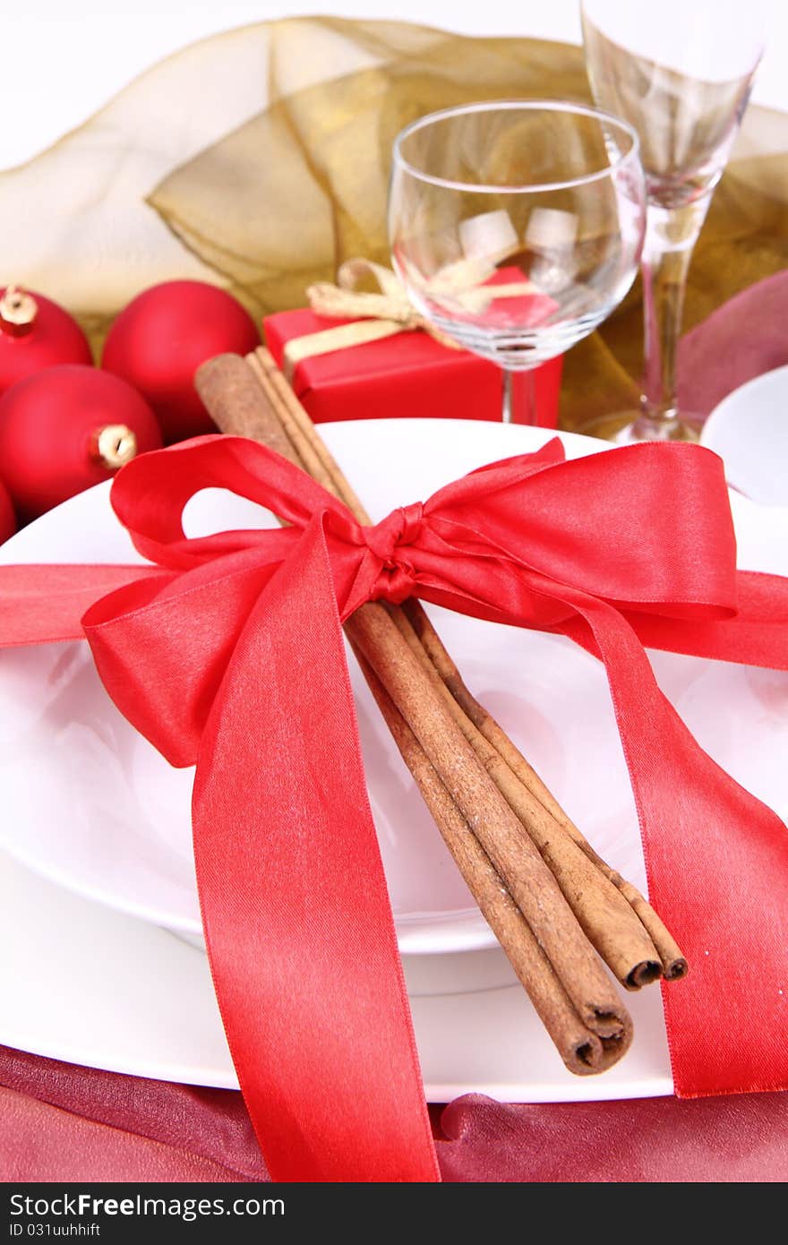 Christmas tableware, decorated with cinnamon sticks, ribbon, christmas balls and a gift in close up. Christmas tableware, decorated with cinnamon sticks, ribbon, christmas balls and a gift in close up