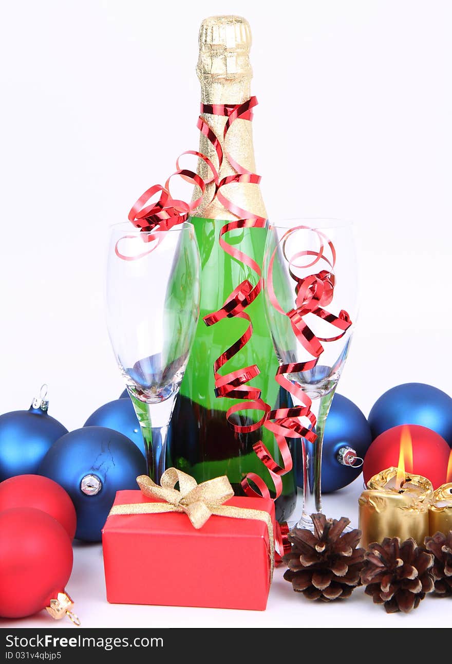 Christmas and New Year's setting - a bottle of champagne, glasses, candles, a gift, and cones on white background