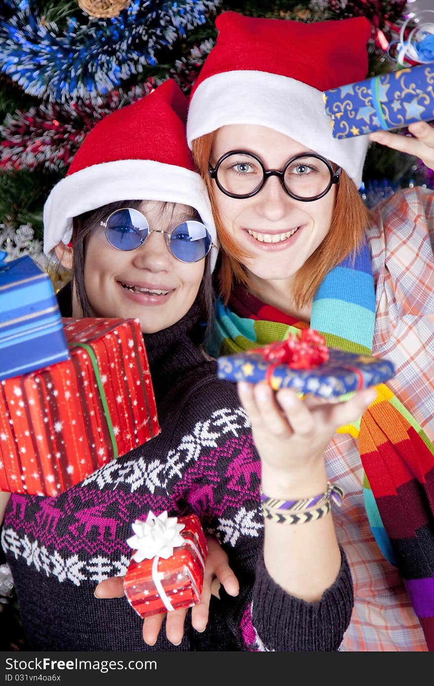 Two beautiful girls with gifts in christmas hats near christmas tree.