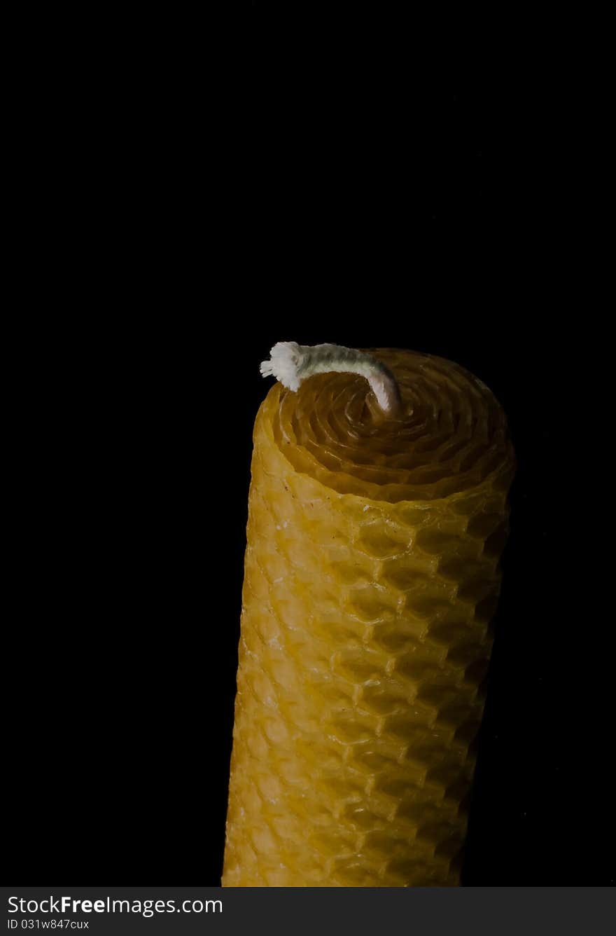 One beeswax candle, isolated on black with fading light