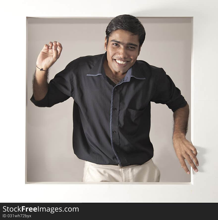 Young indian man, happy in a black short biege pants looking out of a window. Young indian man, happy in a black short biege pants looking out of a window
