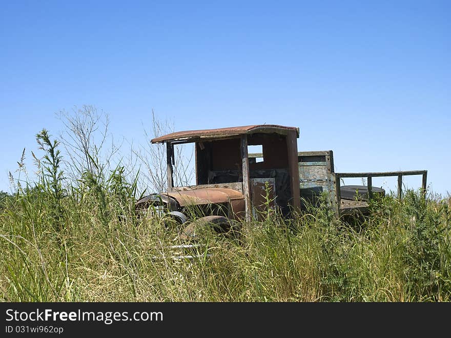 Old rusty truck, abandoned on a land full of weeds, with a blue sky on the background. Old rusty truck, abandoned on a land full of weeds, with a blue sky on the background.