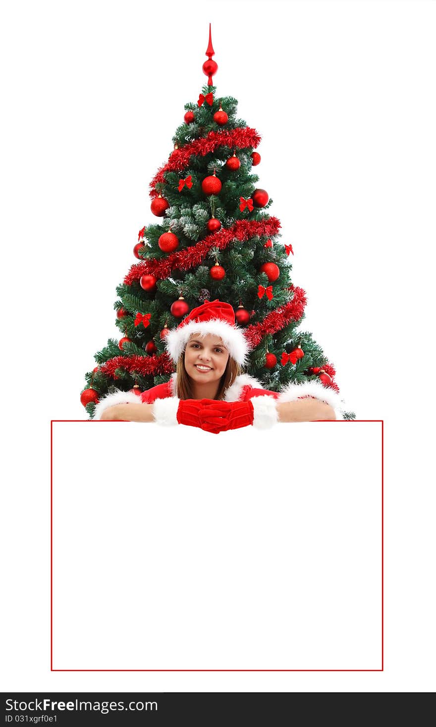 female Santa with red hat and gloves, before the Christmas tree, over a white billboard for your text. female Santa with red hat and gloves, before the Christmas tree, over a white billboard for your text