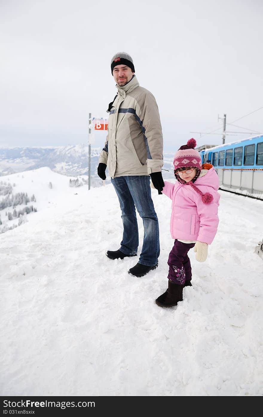 Young father and his daughter in mountains near train in snow winter day