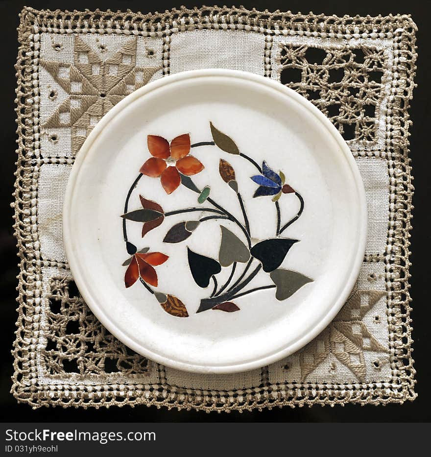 Indian marble plate inlaid of semi precious stones showing flowers. Put on an embroidered  doily. Indian marble plate inlaid of semi precious stones showing flowers. Put on an embroidered  doily