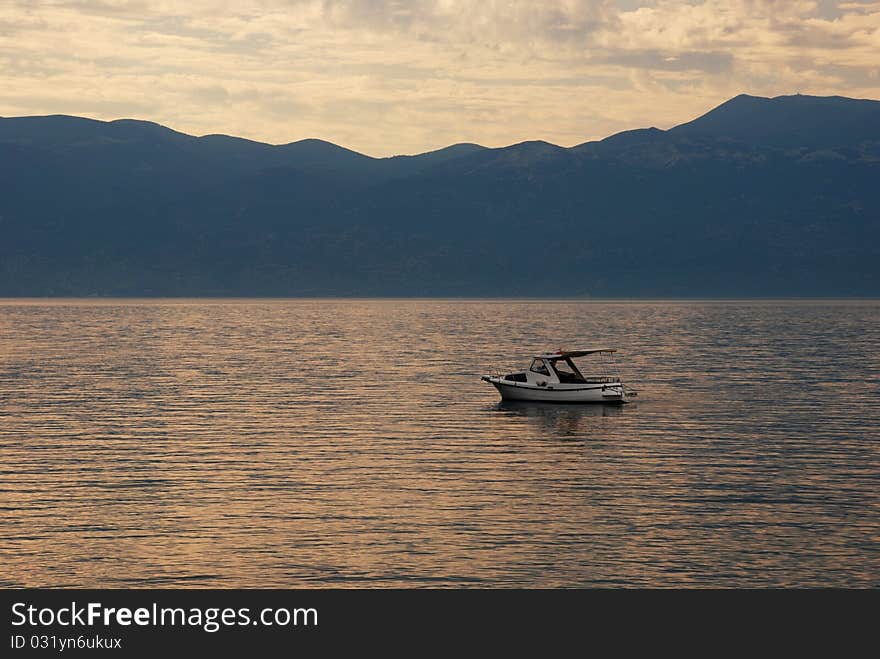 Image of a beautiful sunrise over the hills and a lonely boat on the sea. Image of a beautiful sunrise over the hills and a lonely boat on the sea
