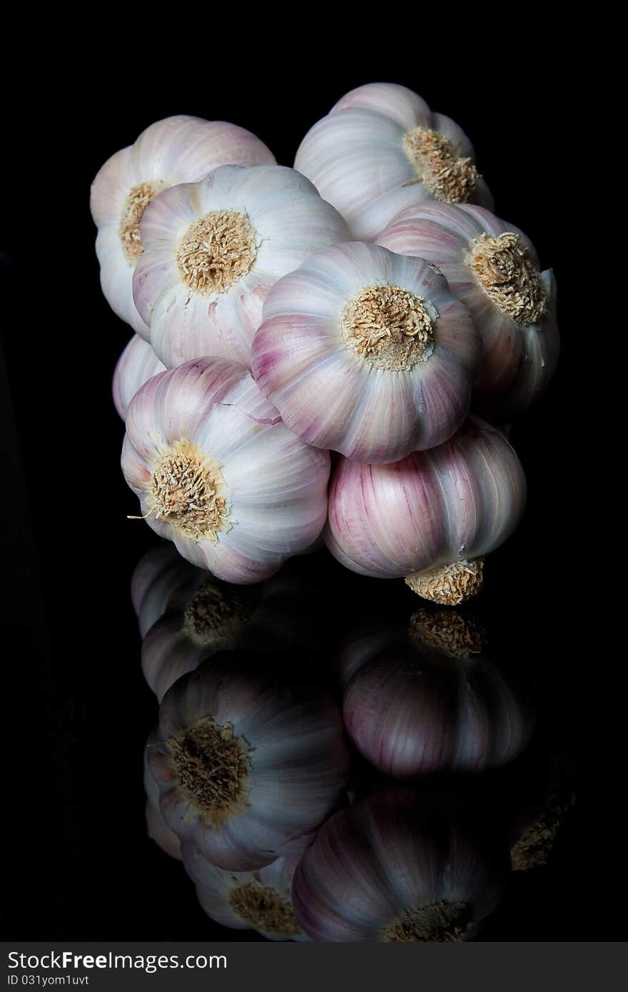 A string of garlic bulbs reflected on a shiny black surface