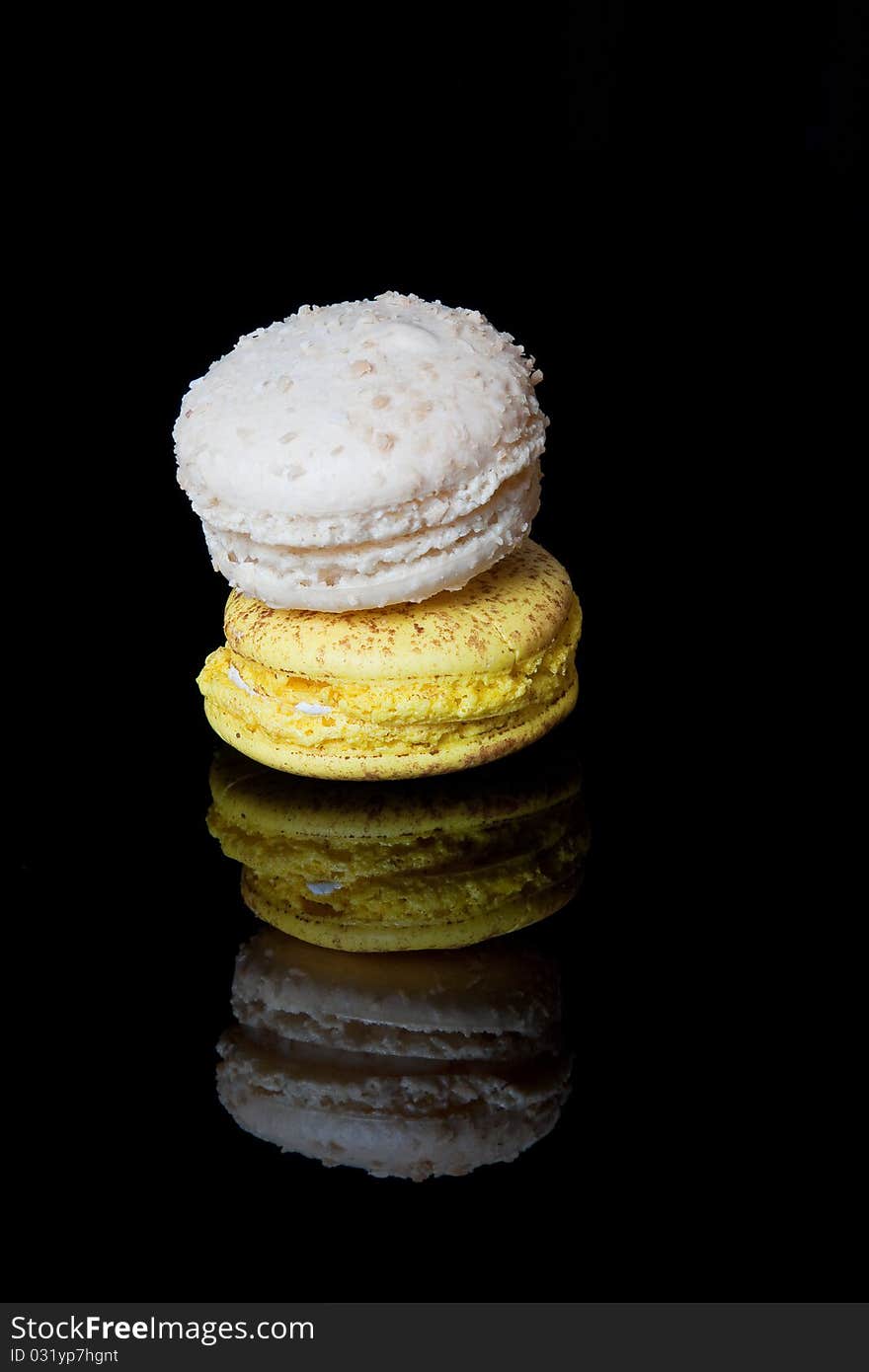 A pair of decorated macaroons reflected in a shiny black surface