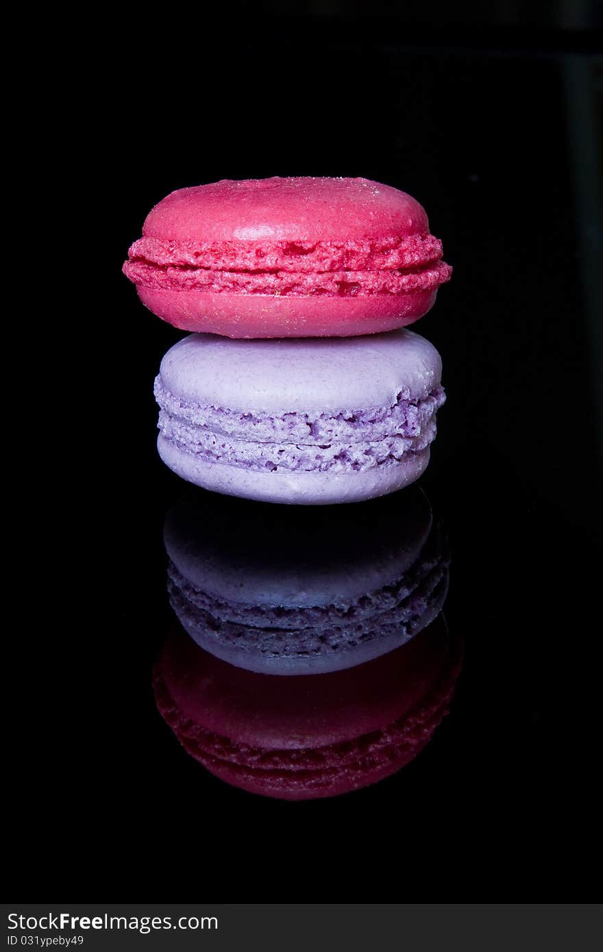 A pair of decorated macaroons reflected in a shiny black surface. A pair of decorated macaroons reflected in a shiny black surface