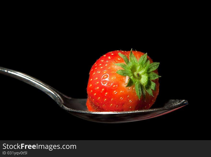 A single strawberry on a metal spoon against a black background