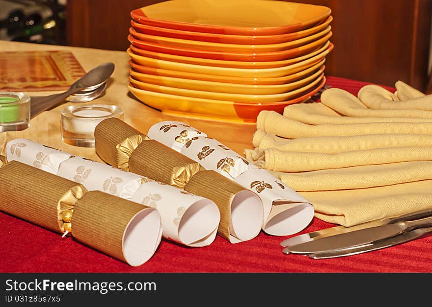 Christmas crackers, napkins, silverware, and stack of plates on a red tablecloth set the mood for a holiday celebration. Christmas crackers, napkins, silverware, and stack of plates on a red tablecloth set the mood for a holiday celebration.