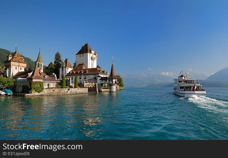 The white tour vessel is passing by a beautiful estate on the coast, against a background of blue sunlighted sky. The white tour vessel is passing by a beautiful estate on the coast, against a background of blue sunlighted sky.