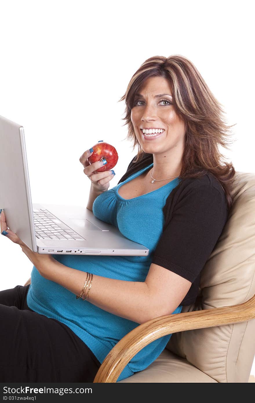 A pregnant business woman sitting and working on her lap top while eating fruit. A pregnant business woman sitting and working on her lap top while eating fruit.