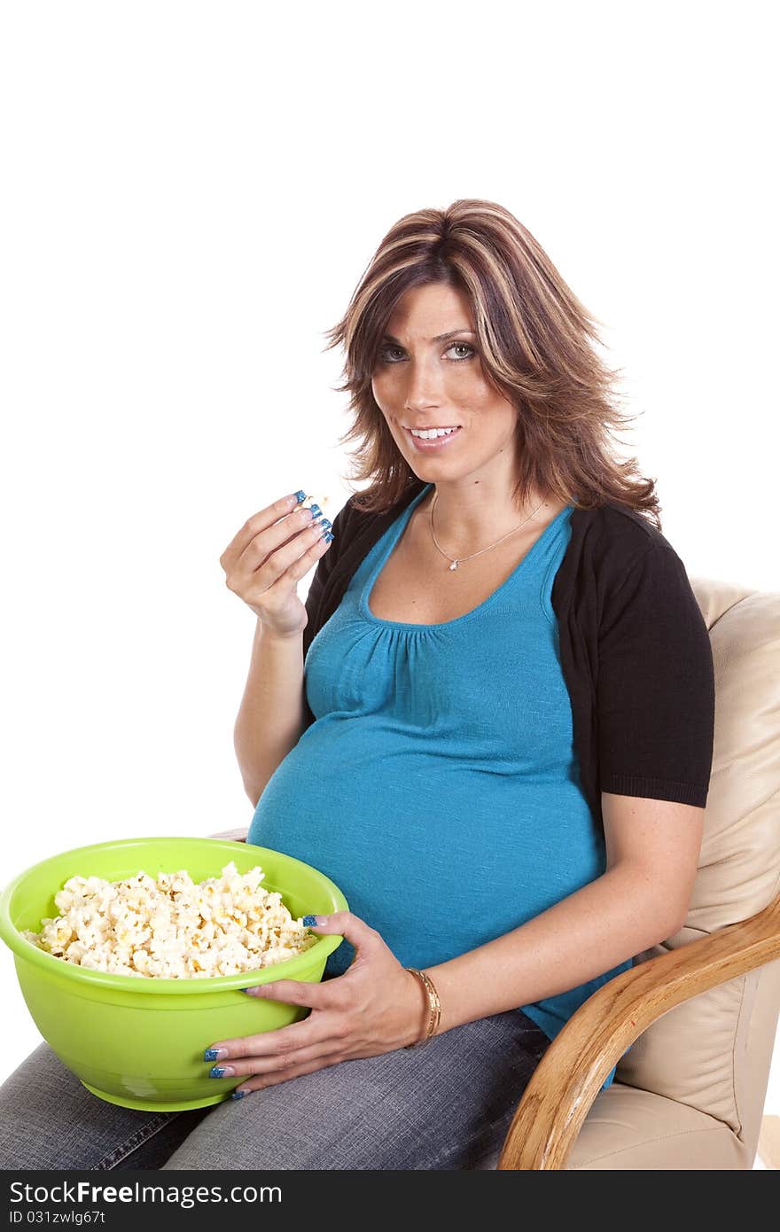 A pregnant woman sitting down eating some popcorn with a happy expression on her face. A pregnant woman sitting down eating some popcorn with a happy expression on her face.