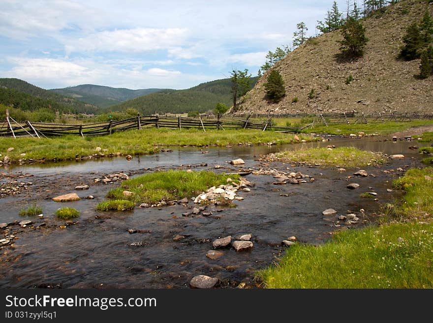 Rocky ford across the river in one village with a fence and some hills on the background