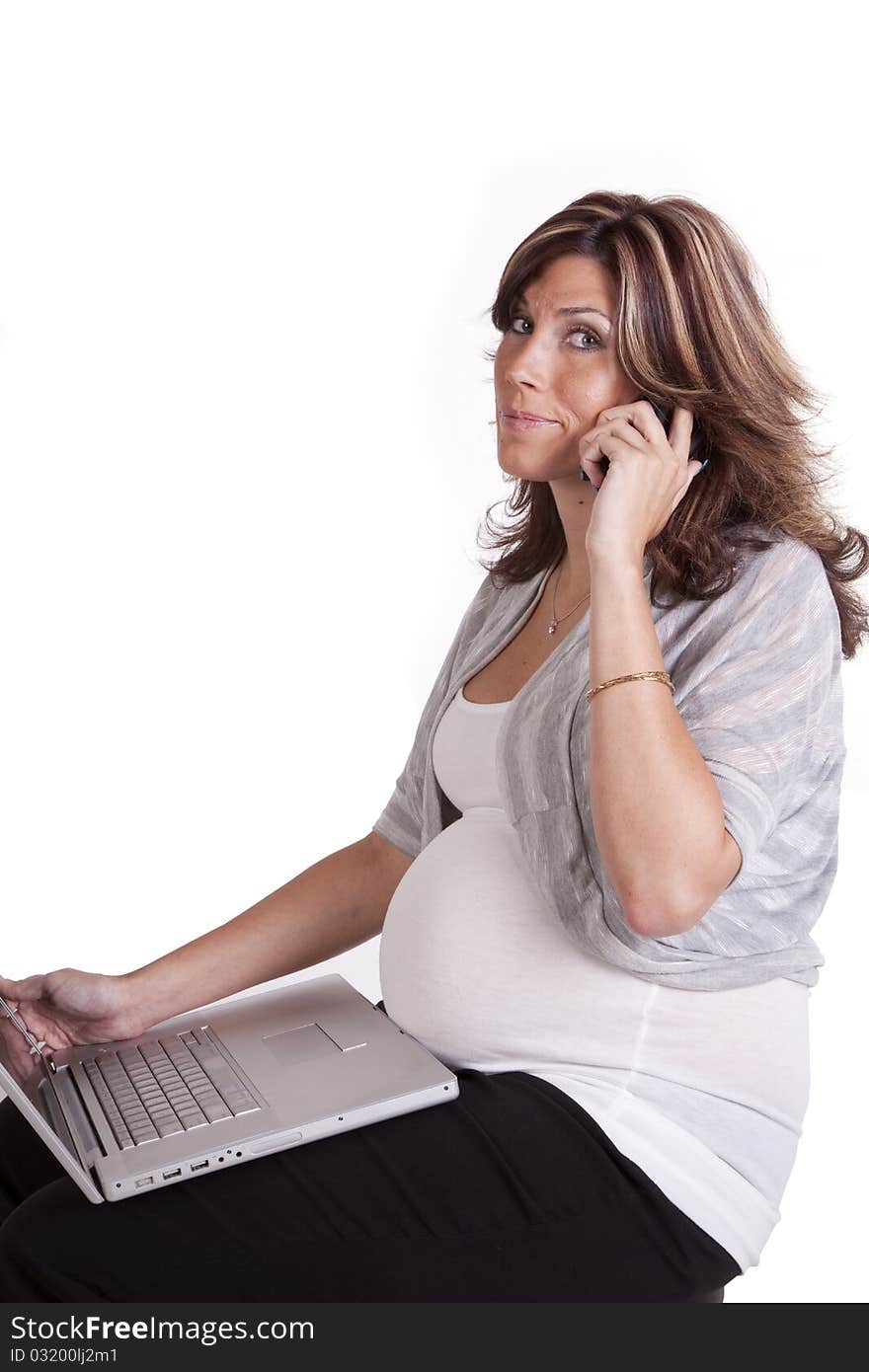 A pregnant business woman sitting and working on her lap top while talking on her phone. A pregnant business woman sitting and working on her lap top while talking on her phone.