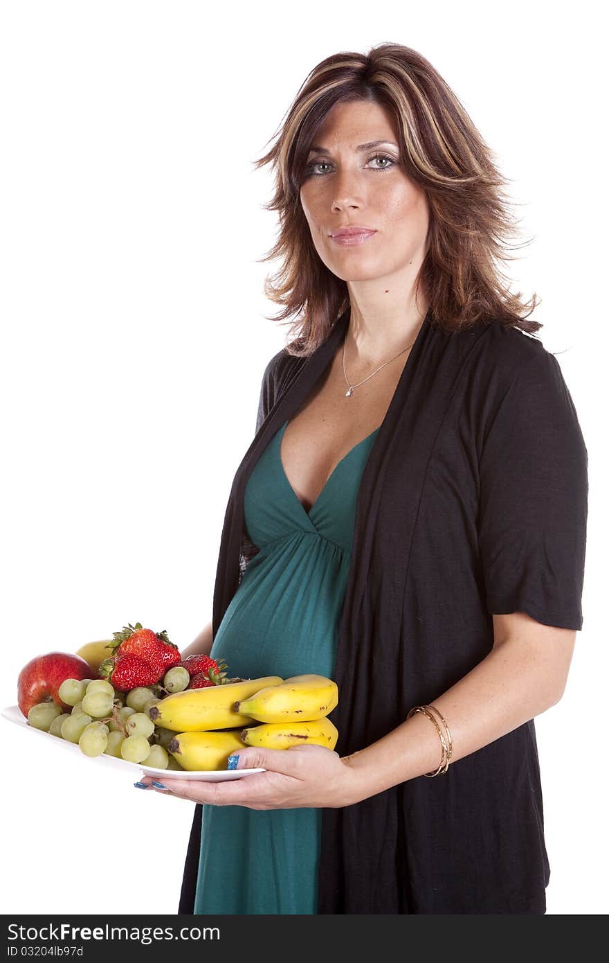 A pregnant woman standing holding a plate of fruit eating healthy for her baby that is in her belly. A pregnant woman standing holding a plate of fruit eating healthy for her baby that is in her belly.