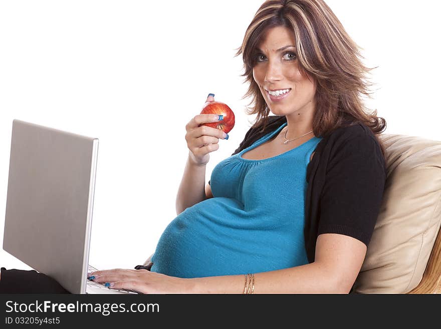 A pregnant business woman sitting and working on her lap top while eating fruit. A pregnant business woman sitting and working on her lap top while eating fruit.