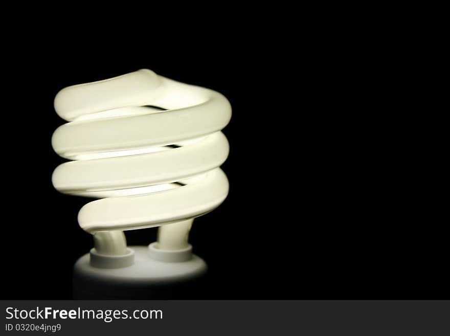 Curly economical environmentally friendly flourescent light bulb that is lighted and on black background. Curly economical environmentally friendly flourescent light bulb that is lighted and on black background