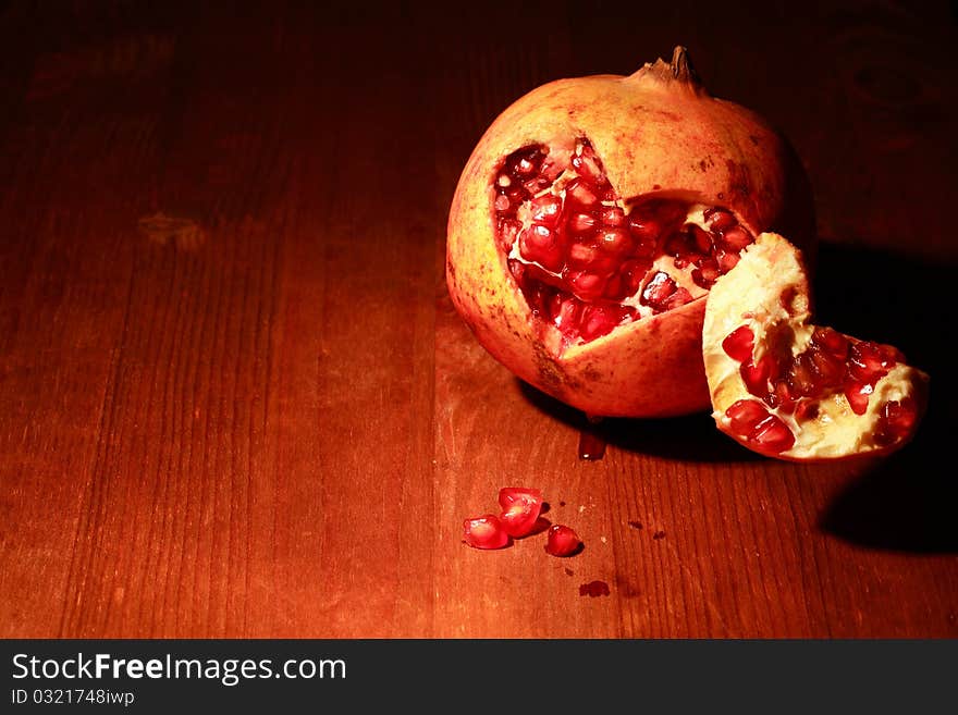 Fresh pomegranate lying on dark wooden background with lighting effect. Fresh pomegranate lying on dark wooden background with lighting effect