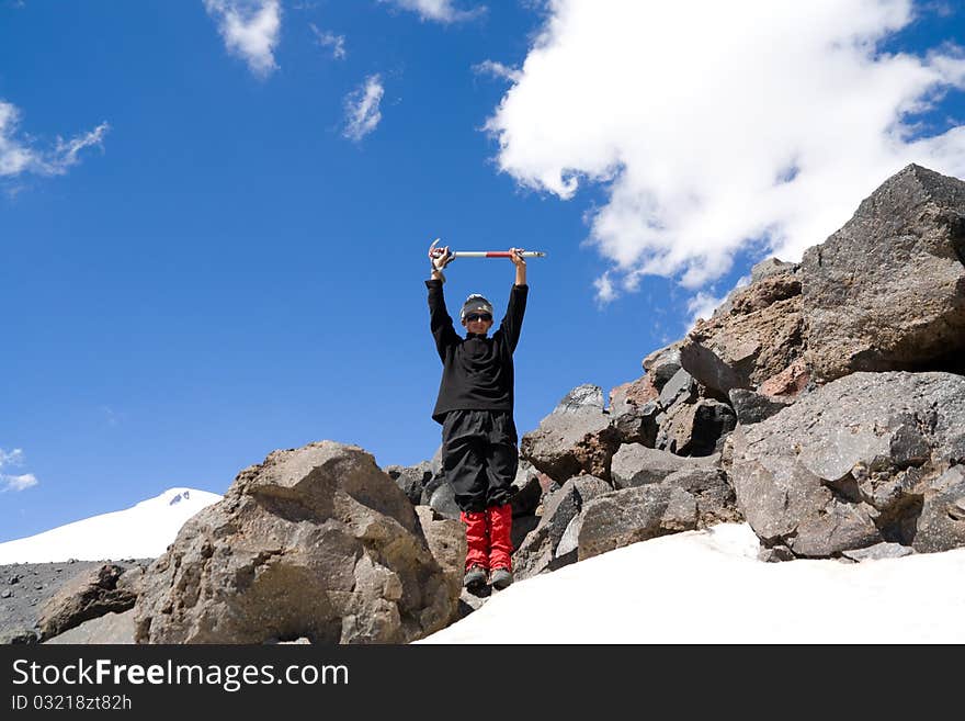 A teenager stands on a mountain with heaved up an above a head ice-axe. A teenager stands on a mountain with heaved up an above a head ice-axe