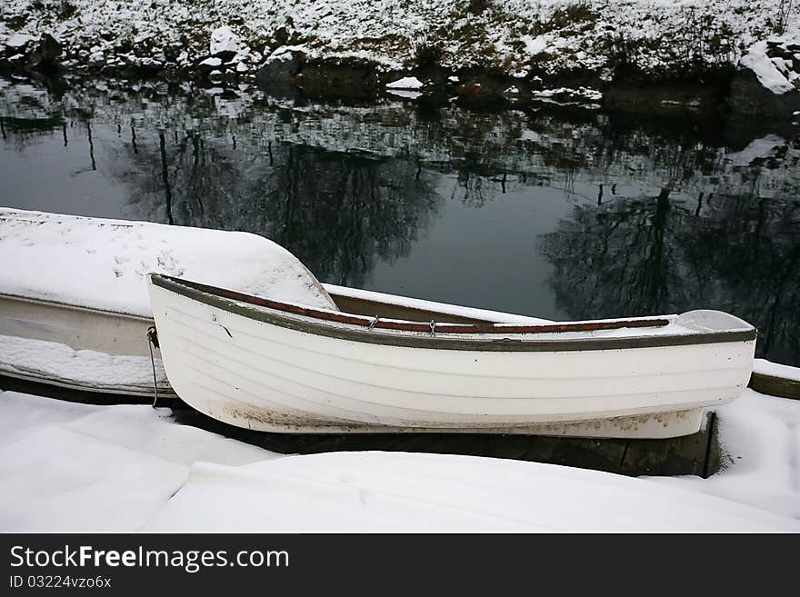 Two rowboats rest in snow on wharf with water and snowy shoreline in background. Two rowboats rest in snow on wharf with water and snowy shoreline in background.