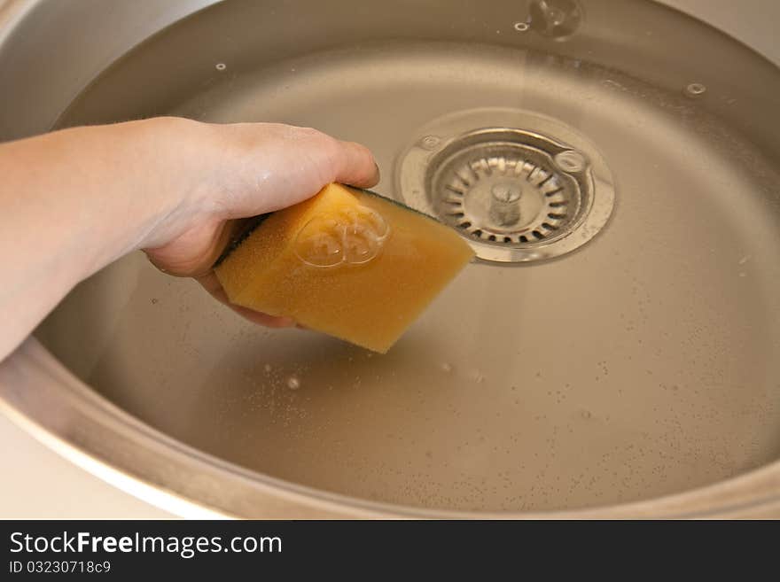 Hand with sponge plunging into the washbasin full of water. Hand with sponge plunging into the washbasin full of water