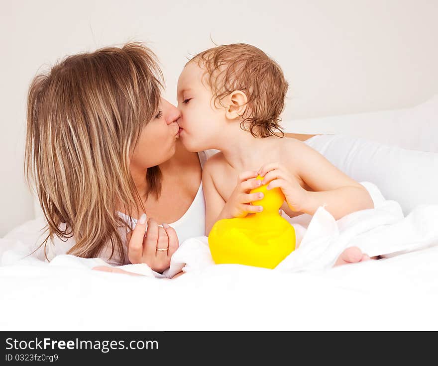 Young beautiful mother and her baby on the bed at home after the shower