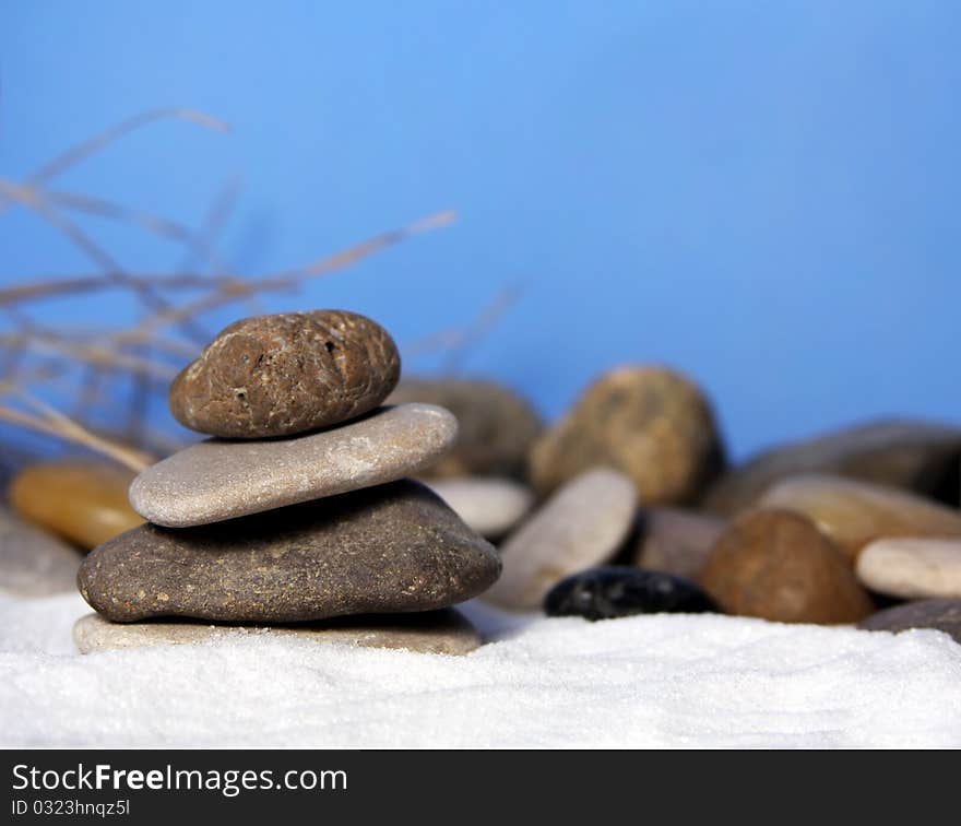 Natural stones stacked on white sand with blue background and grasses. Natural stones stacked on white sand with blue background and grasses