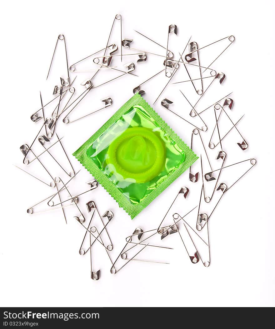 Green condom surrounded by opened metal safety pins. Green condom surrounded by opened metal safety pins