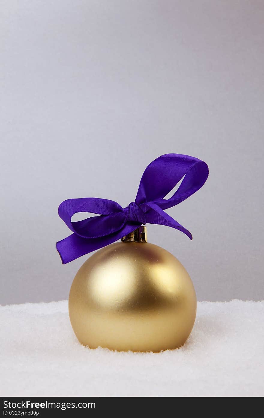 Christmas Golden Ball With Violet Bow And Snow On Silver Background. Christmas Golden Ball With Violet Bow And Snow On Silver Background