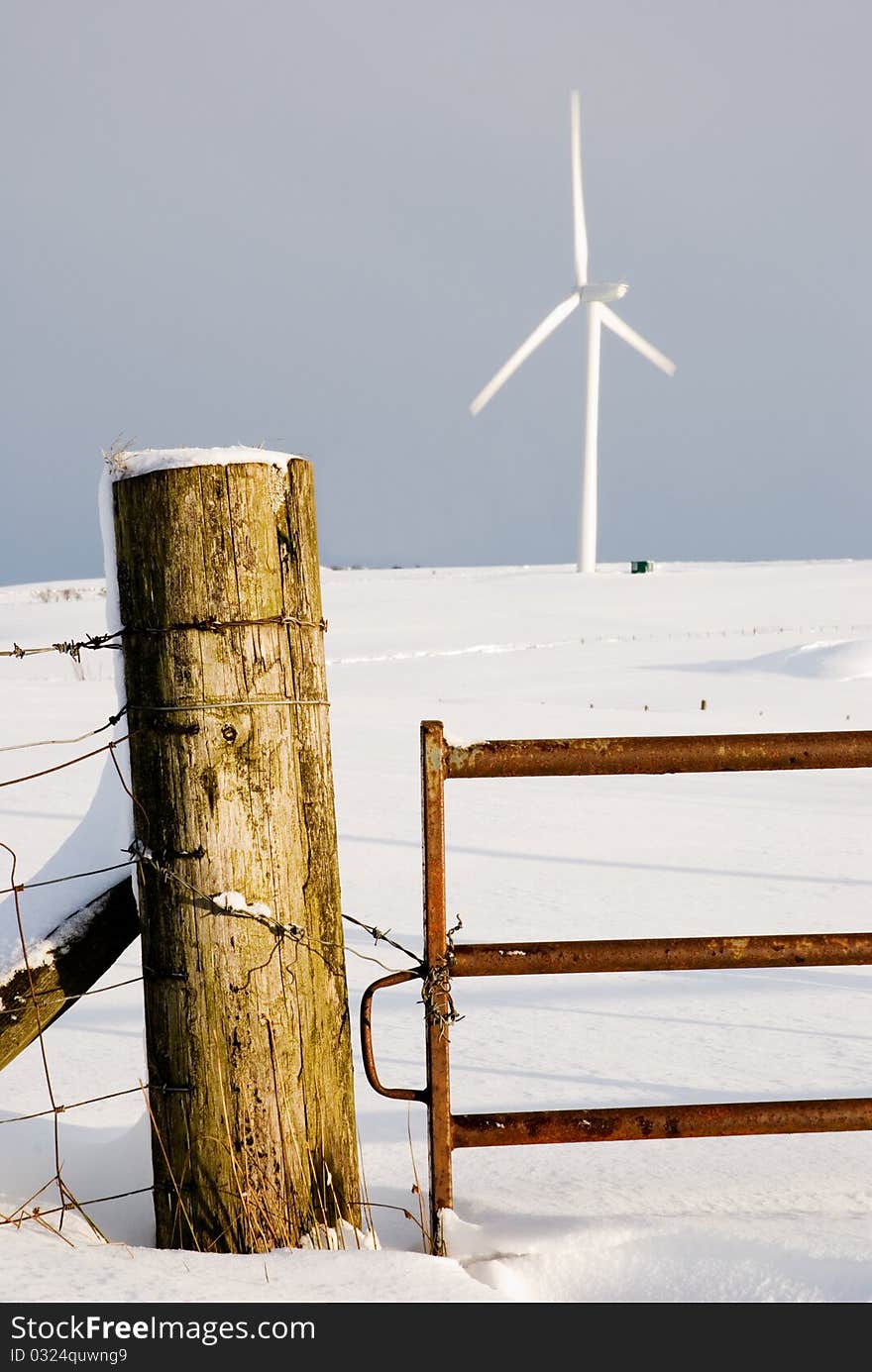 A vertical image of a winter snowscene with gate to a field leading to a wind turbine. A vertical image of a winter snowscene with gate to a field leading to a wind turbine