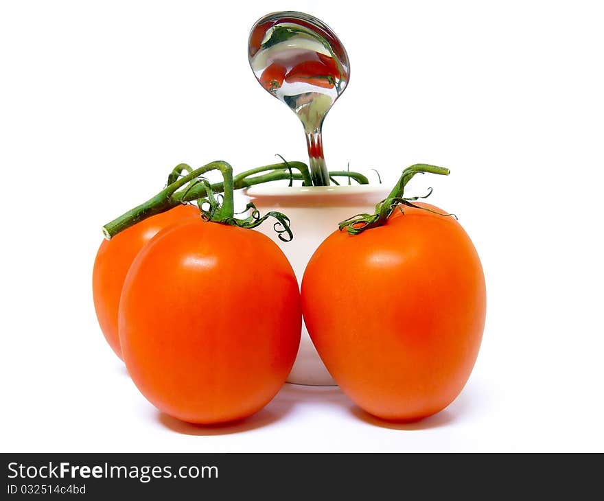 Three tomatoes surounding a white pot with a spoon peeking out. Isolated on a white background. Three tomatoes surounding a white pot with a spoon peeking out. Isolated on a white background