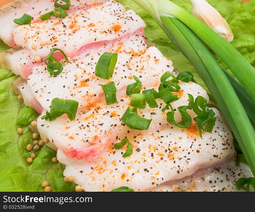 It is thin the cut slices of fat on a plate and decorated with the crushed green onions. It is thin the cut slices of fat on a plate and decorated with the crushed green onions