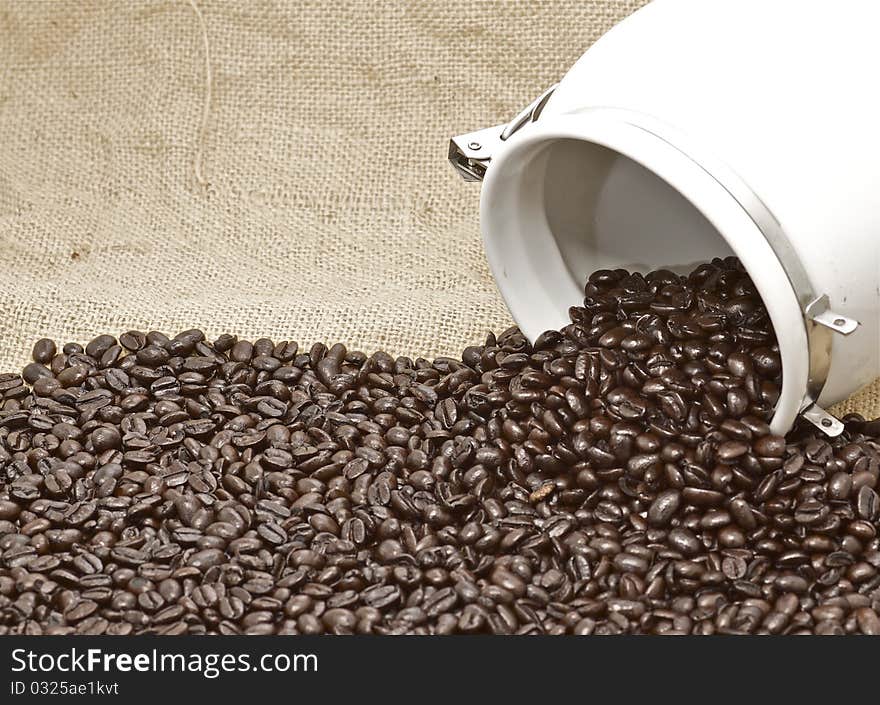 Whole roasted organic coffee beans, evenly spilling out of an urn on a brown burlap background, with an urban vintage retro chic feel. Whole roasted organic coffee beans, evenly spilling out of an urn on a brown burlap background, with an urban vintage retro chic feel.