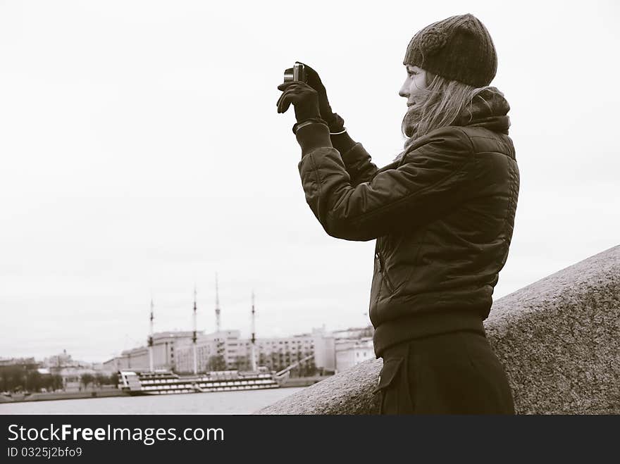 A girl takes pictures a city, upright on the embankment of the river