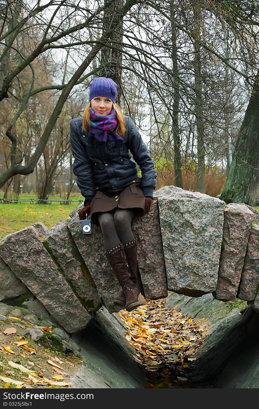 A girl in an autumn city park sits on stone rails. A girl in an autumn city park sits on stone rails