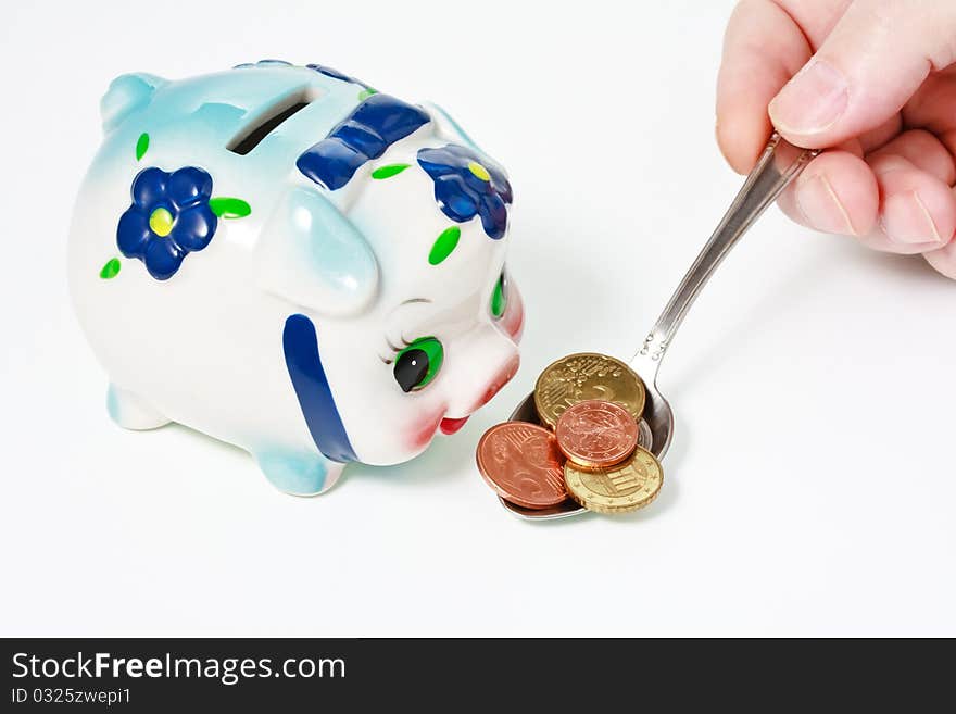 Male hand feeding a colorful piggy bank with a coins in spoon. Male hand feeding a colorful piggy bank with a coins in spoon