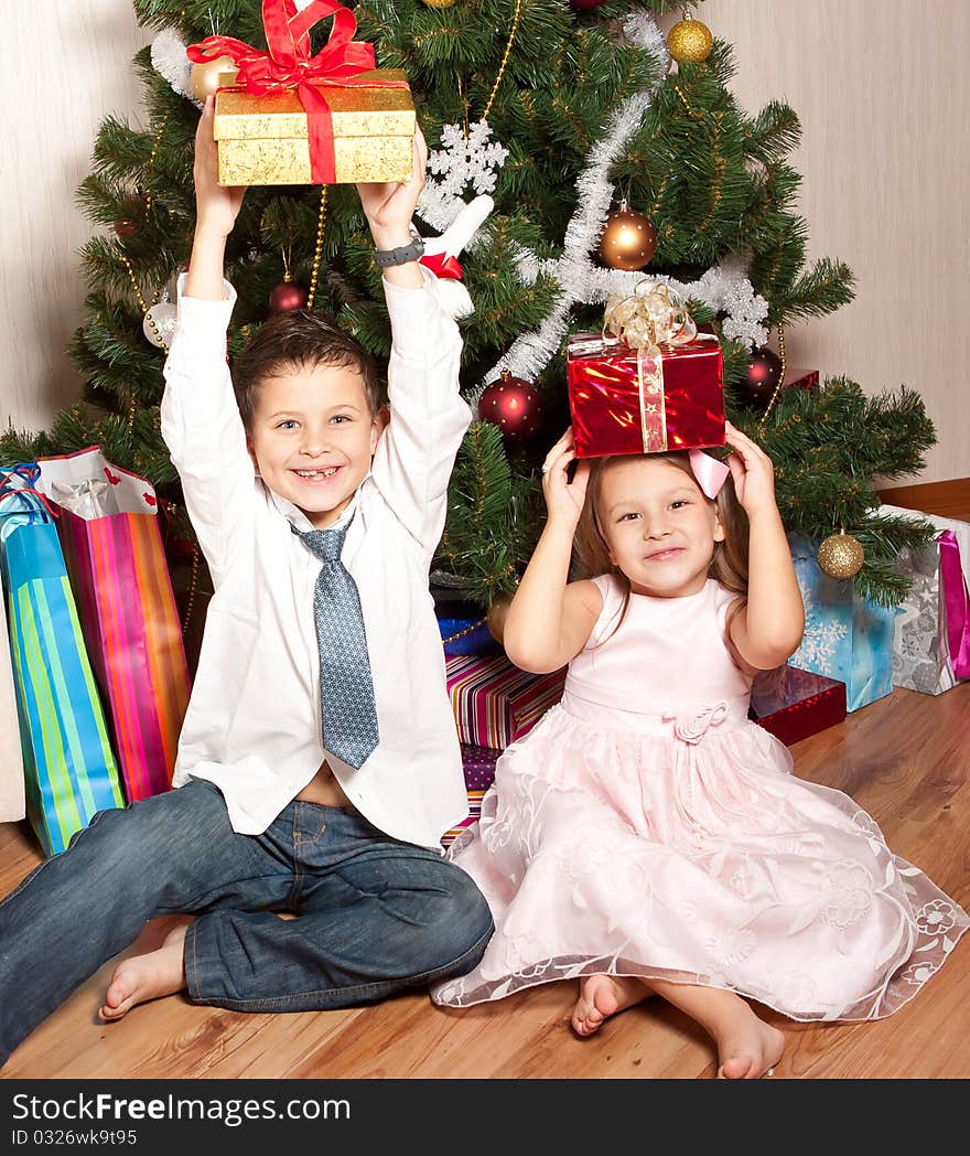 Merry girl and boy with gifts near a new-year tree. Merry girl and boy with gifts near a new-year tree