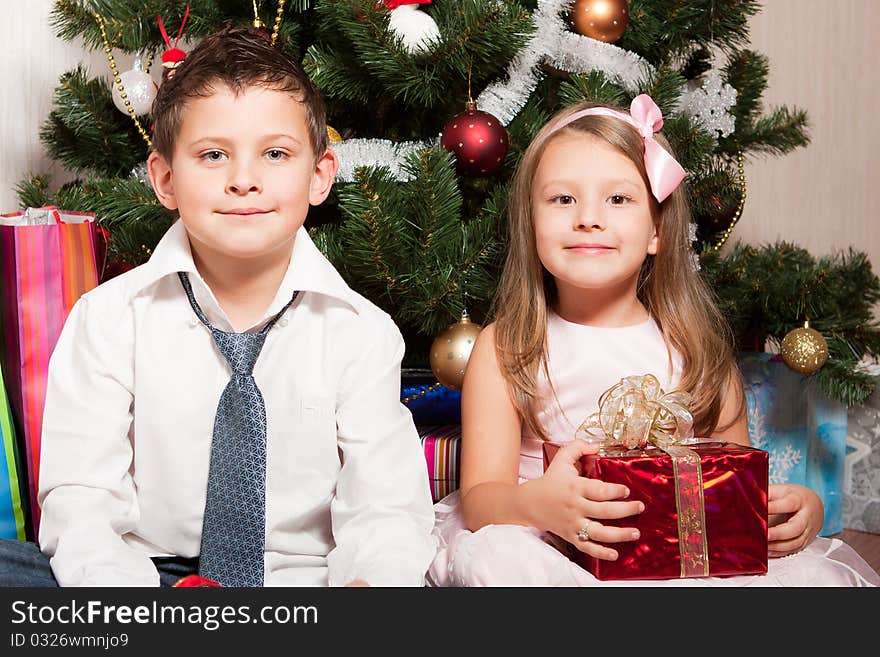 Merry girl and boy with gifts near a new-year tree. Merry girl and boy with gifts near a new-year tree