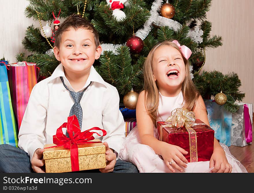 Merry girl and boy with gifts near a new-year tree. Merry girl and boy with gifts near a new-year tree