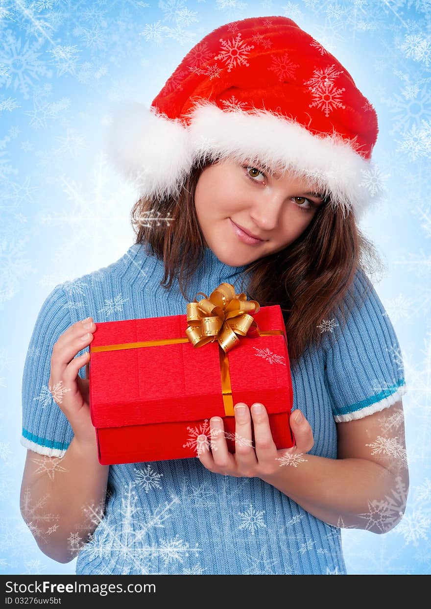 Smiling christmas girl holding gift wearing Santa hat. Blue background with snowflakes.