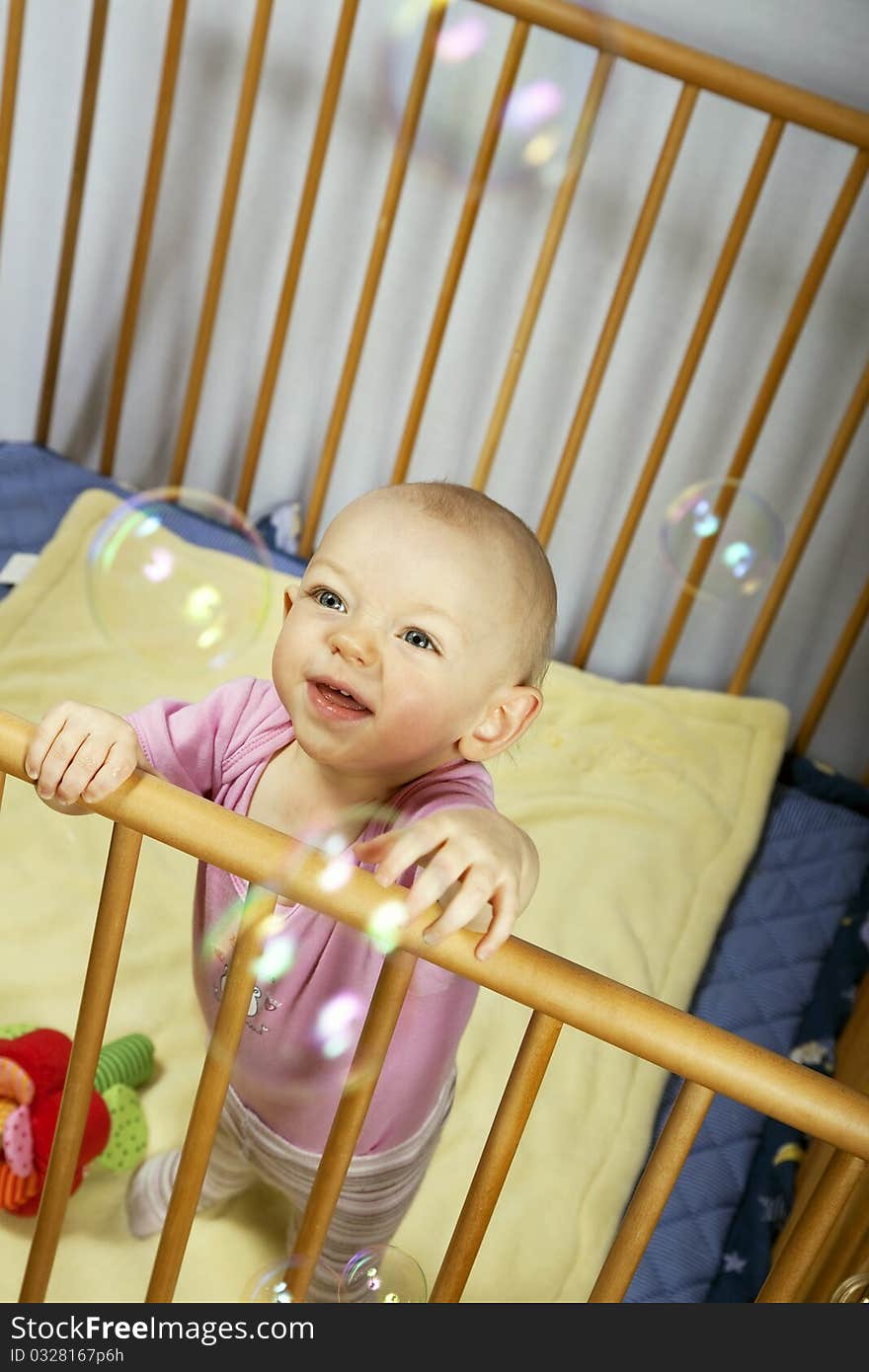 Little baby holds on to the baby bed and is happy about soap bubbles. Little baby holds on to the baby bed and is happy about soap bubbles