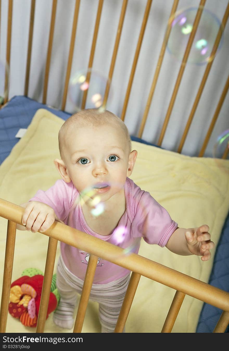 Little baby holds on to the baby bed and looks behind the bubbles. Little baby holds on to the baby bed and looks behind the bubbles