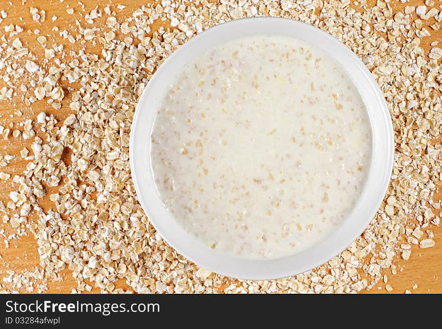 A big bowl of cooked oatmeal with oatmeal flakes from top point of view