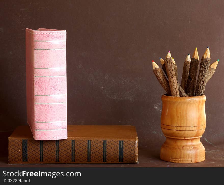 Old school books and wooden pencils on brown background